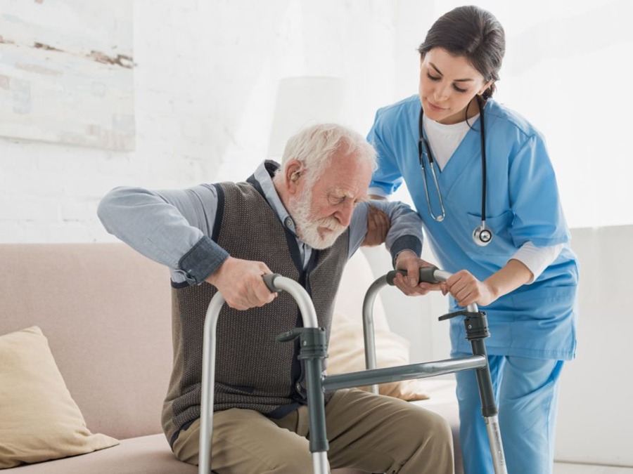 Aid helping older man stand up to use walker