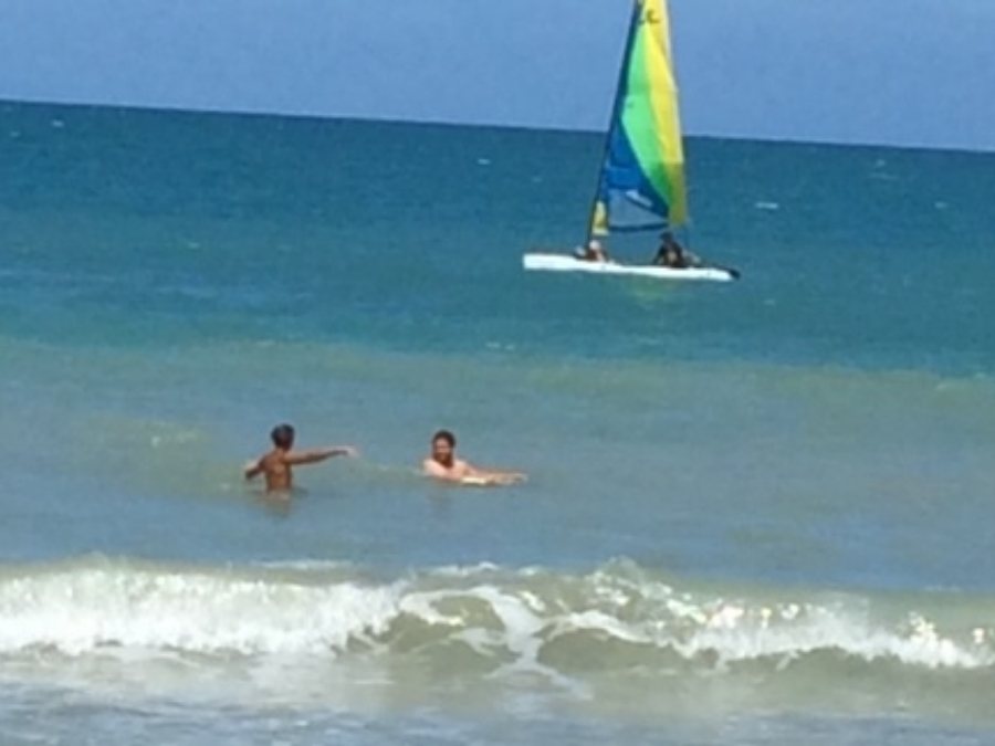Two young men playing in the surf with a windsurfer behind them in Atlantic Ocean in Vero Beach, FL