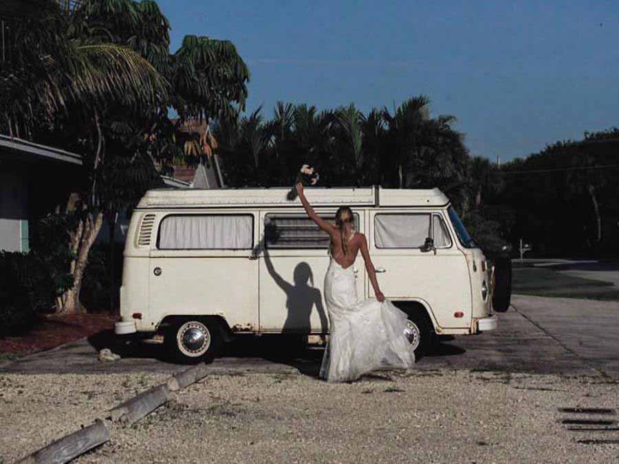 Woman in wedding gown standing by van