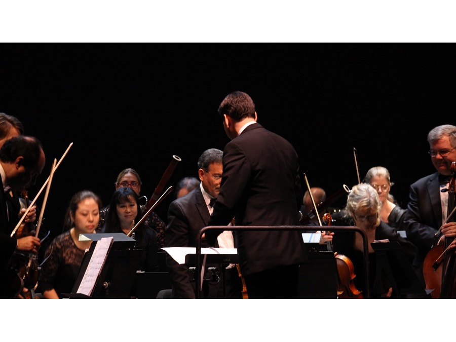 Photo of Maestro David Amado conducting the Atlantic Classical Orchestra on stage.							